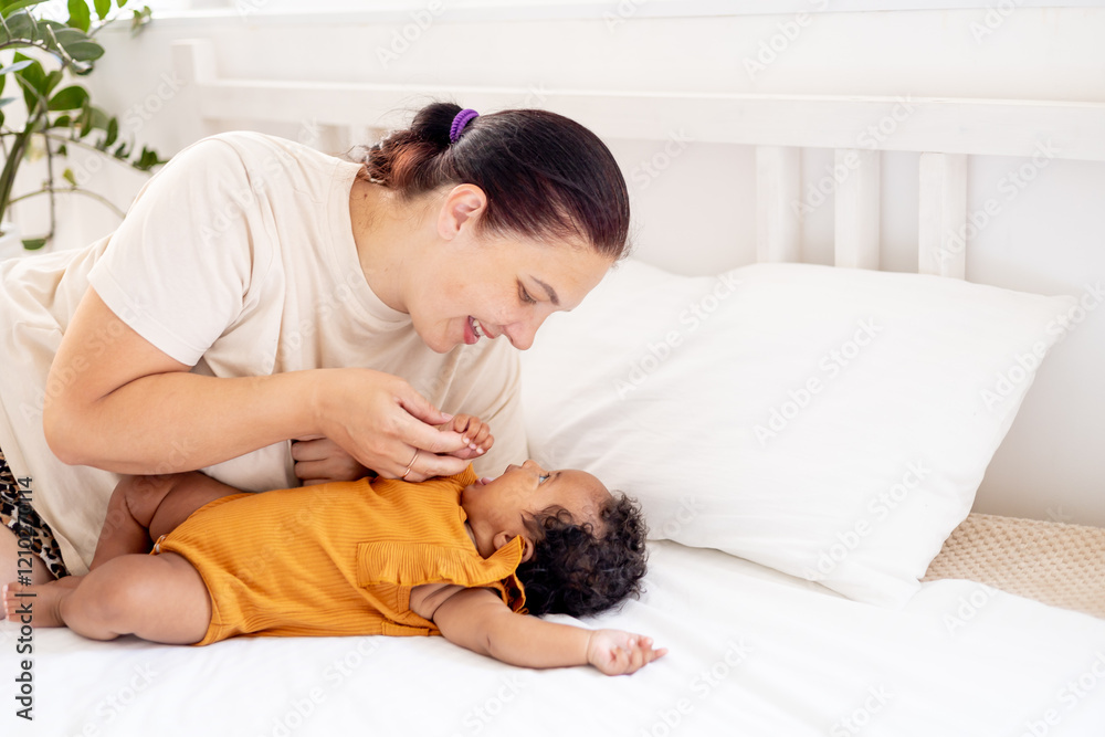 a little African-American baby girl in an orange bodysuit on the bed at home, a funny six-month-old black newborn baby hugs a stuffed rabbit and smiles. View from above a little African-American baby girl in an orange bodysuit on the bed at home, a funny six-month-old black newborn baby hugs a stuffed rabbit and smiles. View from above