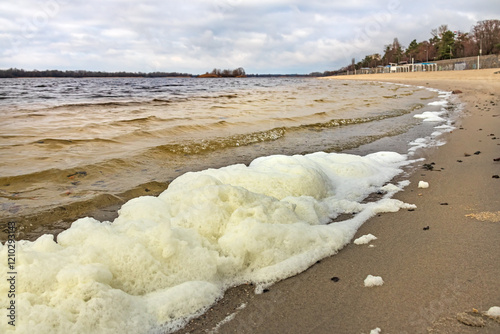 White foam on the bank of the Dnieper river (Dnipro) in Kremenchuk city, cloudy windy day photo