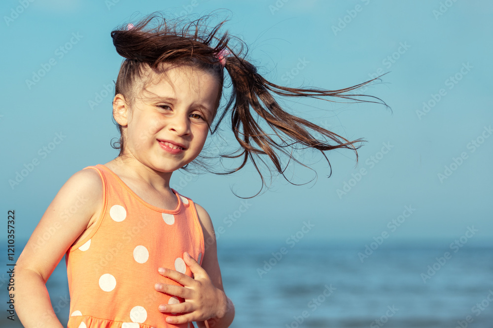 Portrait of a happy little girl with flying hair walking on the beach in summer