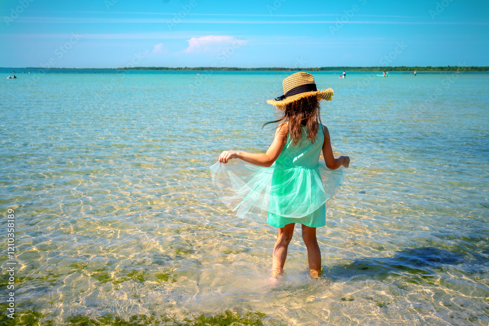 Happy little girl walking on the beach in summer. Child in a blue dress and straw hat