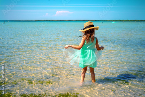 Obraz na płótnie Happy little girl walking on the beach in summer. Child in a blue dress and straw hat w salonie