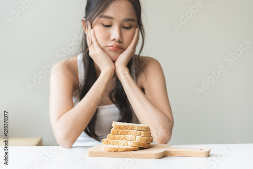 Gluten allergy, asian young woman, girl refusing to eat, looking at bread slice on plate in breakfast food meal on table at home, having a stomach ache. Gluten intolerant and Gluten free diet concept. photo