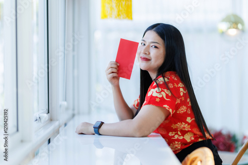 Portrait of happy asian woman relaxing wearing red cheongsam dress holding red envelopes at home in the living room indoor decoration for Chinese new year festival celebrate culture of china holiday