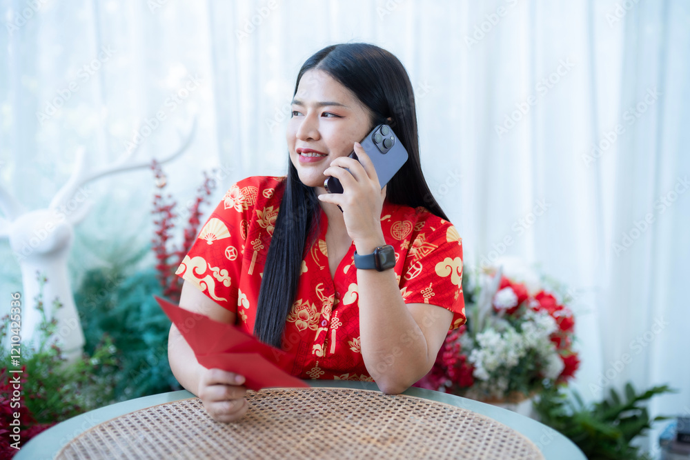 Portrait of asian woman wearing red cheongsam dress holding red envelopes and smartphone at home in the living room indoor decoration for Chinese new year festival celebrate culture of china holiday