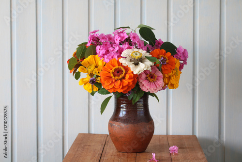 Colorful bouquet of zinnia and phlox flowers standing in a clay vase on a wooden table