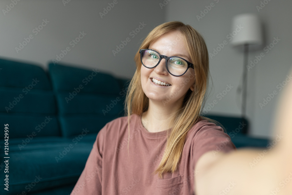 Petty blond woman 30s wearing pink t-shirt smiling while looking at camera and taking selfie photo in living room. Online communication concept. High quality photo