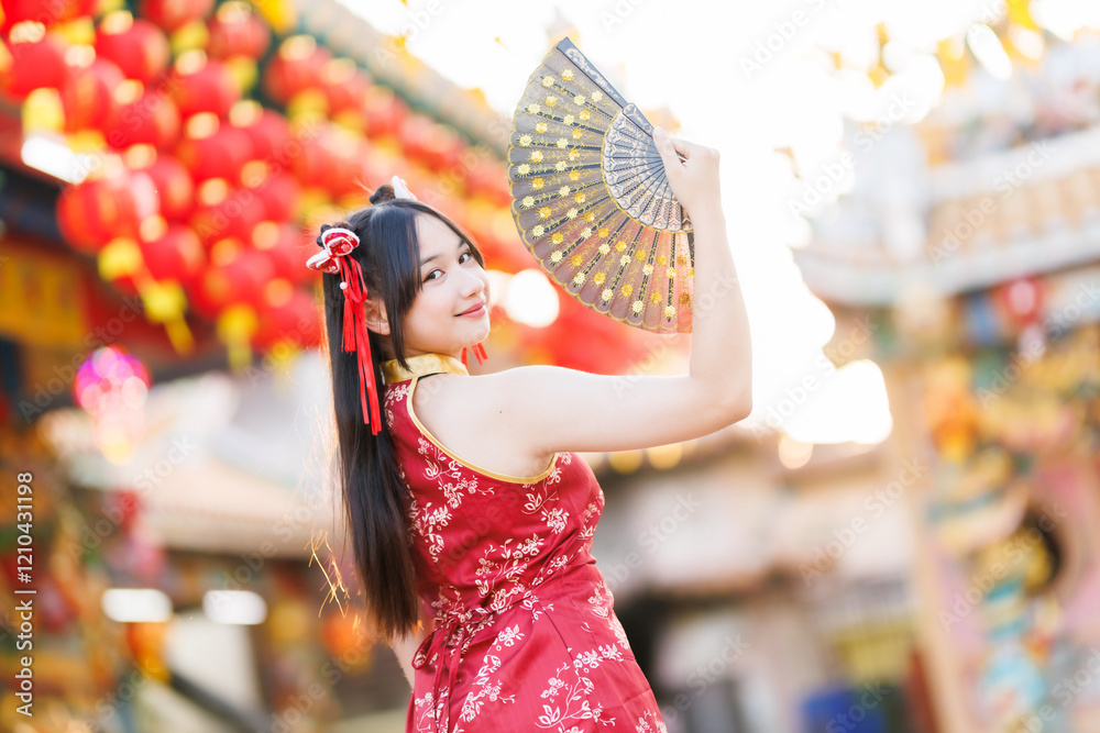 Portrait beautiful cute smiles Asian young woman wearing red traditional Chinese cheongsam decoration and holding a Chinese Fanning for Chinese New Year Festival at Chinese shrine in Thailand