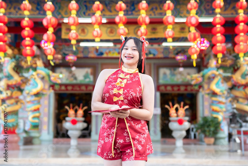 Obraz na płótnie Portrait beautiful cute smiles Asian young woman wearing red traditional Chinese cheongsam decoration and holding a Chinese Fanning for Chinese New Year Festival at Chinese shrine in Thailand w salonie