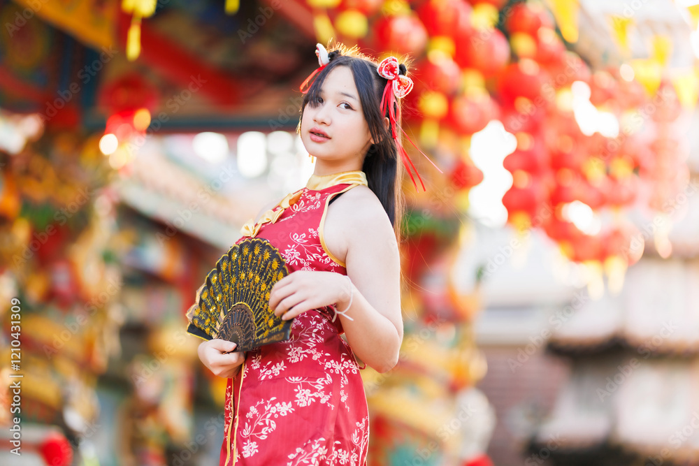 Portrait beautiful cute smiles Asian young woman wearing red traditional Chinese cheongsam decoration and holding a Chinese Fanning for Chinese New Year Festival at Chinese shrine in Thailand