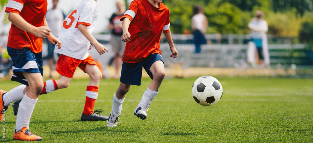 Boys play football game during youth football league. Players in speed duel. Kids have fun in sports match. Soccer boys kicking a ball on grass turf. Kids in red and white soccer jersey shirts Boys play football game during youth football league. Players in speed duel. Kids have fun in sports match. Soccer boys kicking a ball on grass turf. Kids in red and white soccer jersey shirts