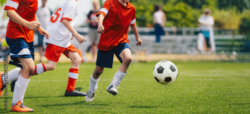 Boys play football game during youth football league. Players in speed duel. Kids have fun in sports match. Soccer boys kicking a ball on grass turf. Kids in red and white soccer jersey shirts