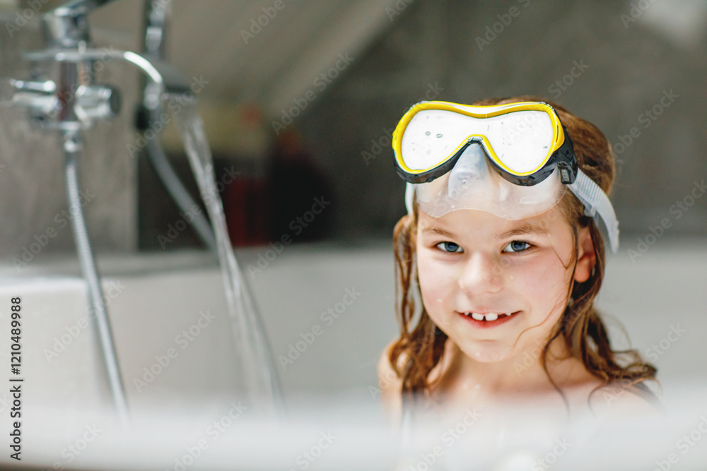 Litltle girl taking a bath with a foam in bathtub. Happy child having fun with swimming mask