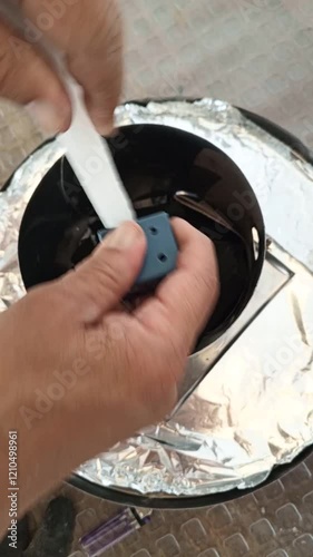 A man scrapes wax from a candle inside a cylinder with charcoal; initial process of lighting a smoker barrel.
