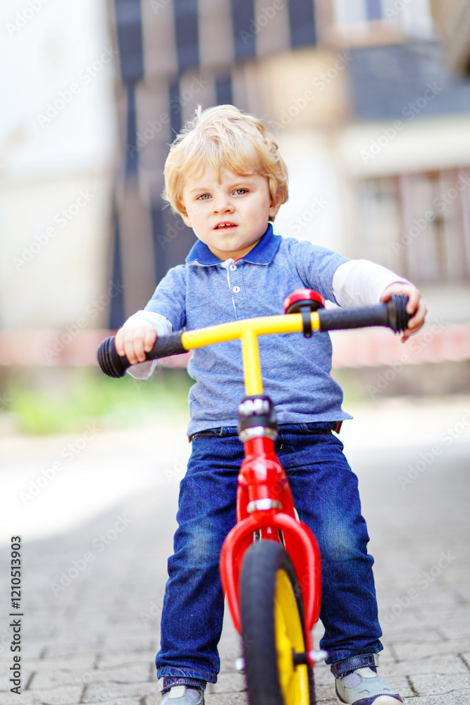 Active blond kid boy in colorful clothes driving balance and learner's bike or bicycle in domestic garden. Toddler child dreaming and having fun on warm summer day. outdoors movement game for children Active blond kid boy in colorful clothes driving balance and learner's bike or bicycle in domestic garden. Toddler child dreaming and having fun on warm summer day. outdoors movement game for children