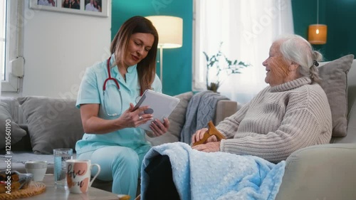 A smiling female doctor with a digital tablet talks to a cheerful senior woman during a medical home visit.