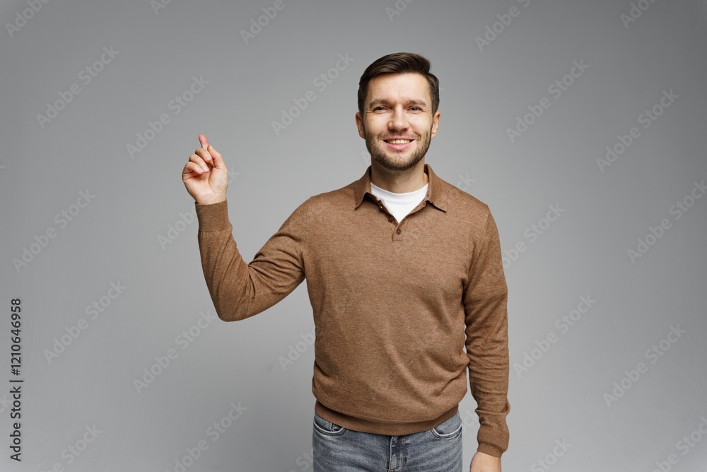 Man smiling while pointing upwards in a neutral studio setting during daytime