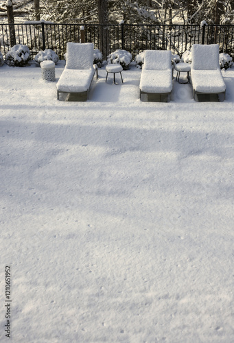 poolside lounge chairs covered in snow during winter (off season spa patio back yard) pool loungers side tables snowy blizzard closed season (recliner reclining chair) end of year photo