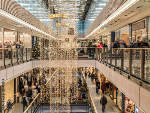 A bustling shopping mall adorned with holiday lights and decorations, filled with customers enjoying the festive ambiance while browsing the variety of retail stores