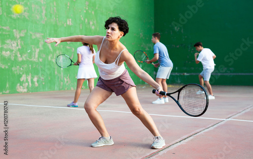 Active fit young hispanic woman playing frontenis on open court on summer day, hitting ball with strung tennis racquet to score to opposing team. Popular Spanish sports.. photo