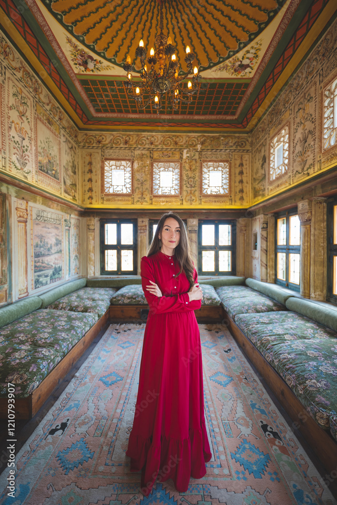 Fototapeta premium a beautiful girl in a long red dress poses in a room with a traditional Turkish interior