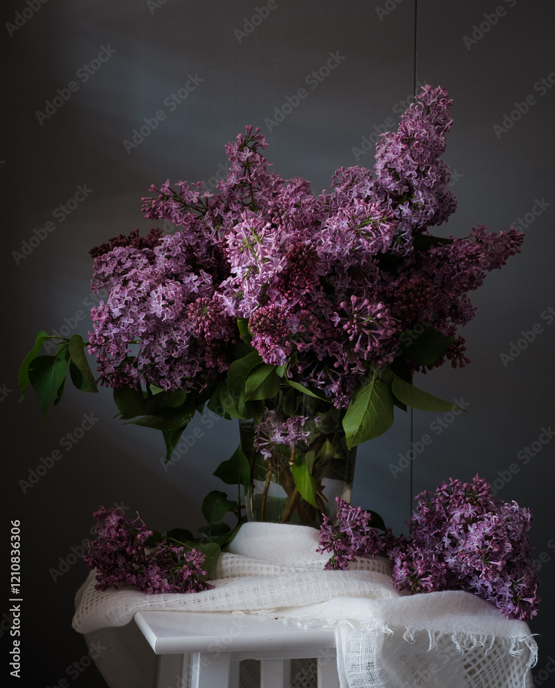 A beautiful arrangement of lilac flowers is displayed in a white vase on a table. The flowers are in full bloom and their vibrant color creates a sense of freshness and vitality.