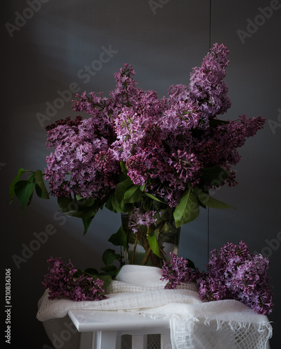Obraz na płótnie A beautiful arrangement of lilac flowers is displayed in a white vase on a table. The flowers are in full bloom and their vibrant color creates a sense of freshness and vitality. w salonie