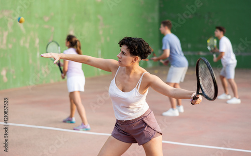 Active fit young hispanic woman playing frontenis on open court on summer day, hitting ball with strung tennis racquet to score to opposing team. Popular Spanish sports.. photo