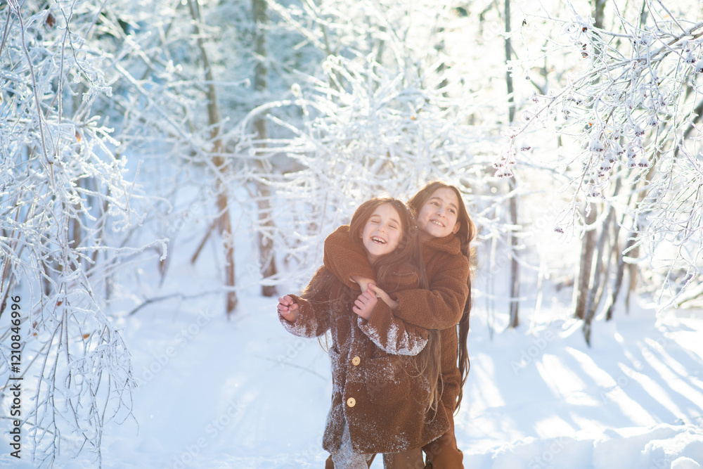 Fototapeta premium Happy funny little girls in the forest with ice trees. Children smiling, hugging, walking through the snow outdoors in the forest