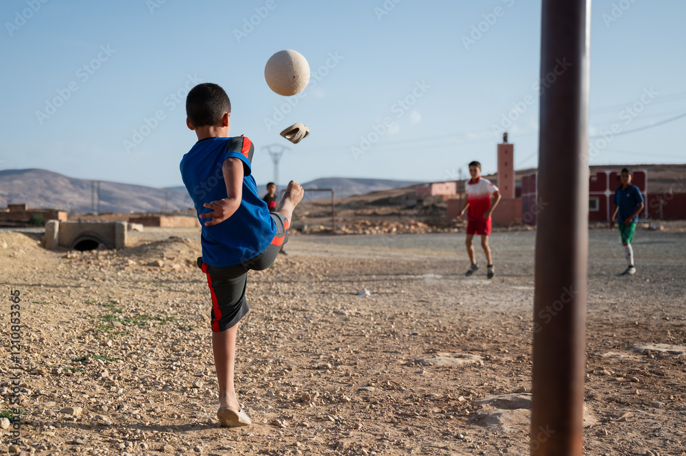 A boy in flip-flops kicks the ball during a game of football in a Moroccan village.
