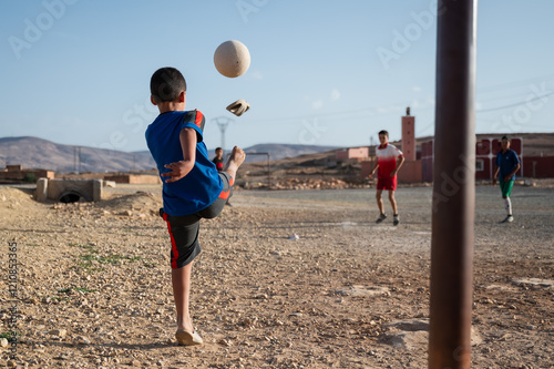 Obraz na płótnie A boy in flip-flops kicks the ball during a game of football in a Moroccan village. w salonie