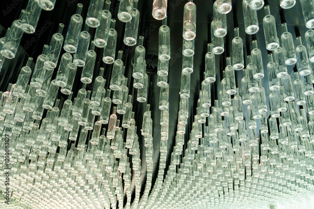 Obraz premium This artistic installation features a captivating collection of glass bottles suspended from the ceiling, creating a unique visual experience that transforms the gallery space.