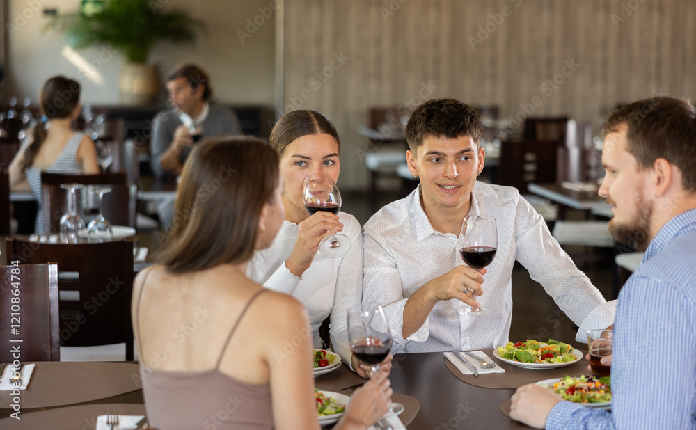 Two couples meet for dinner at restaurant. They chat and drink red wine Two couples meet for dinner at restaurant. They chat and drink red wine