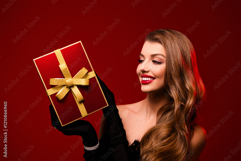 Photo of happy smiling lady holding showing cirtmas present with yellow bow looking on red color background Photo of happy smiling lady holding showing cirtmas present with yellow bow looking on red color background