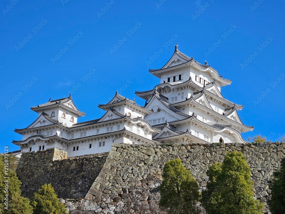Himeji Castle, a pristine white Japanese castle with intricate tiered roofs, perched on a stone foundation, surrounded by greenery, and set against a bright blue sky. Himeji Castle, a pristine white Japanese castle with intricate tiered roofs, perched on a stone foundation, surrounded by greenery, and set against a bright blue sky.