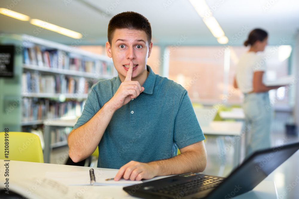 Obraz premium Young man calls for silence in the public library - puts his index finger to his lips