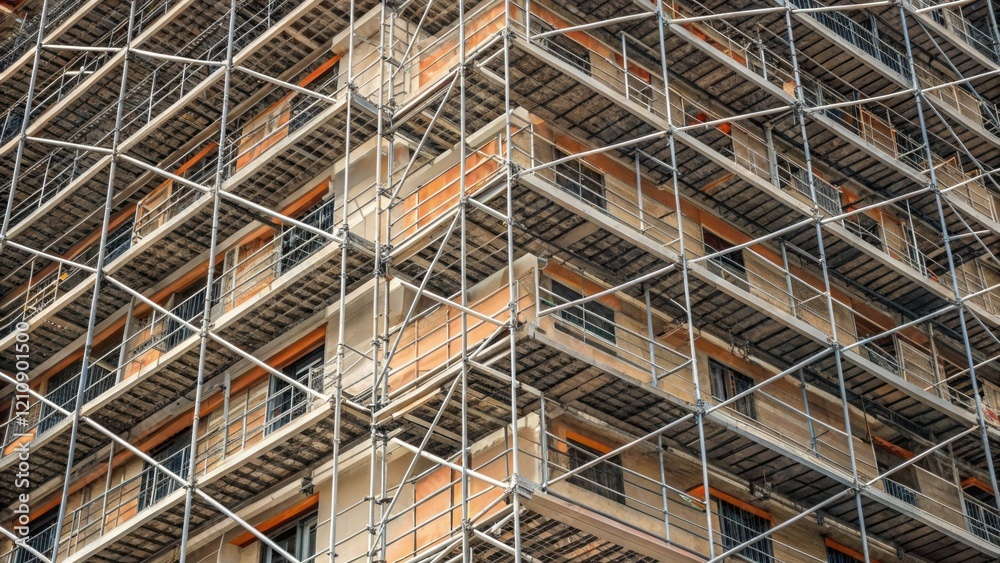 Obraz premium A medium closeup image revealing the intricate patterns of scaffolding surrounding a multistory building highlighting the geometric alignment of platforms and safety nets.