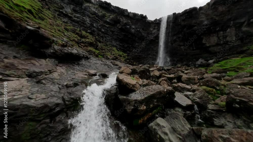 A scenic aerial view of a tall waterfall in a rocky canyon in the Faroe Islands