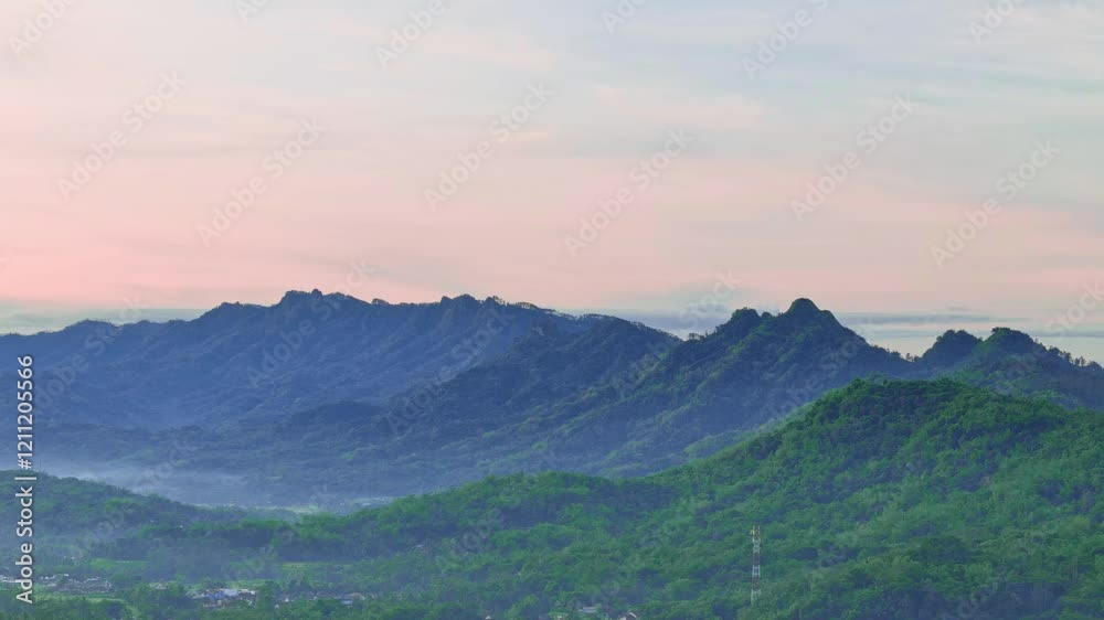 Aerial view of mountain range, valleys with dense forests in a slightly foggy morning and sunrise sky. Indonesia nature landscape. Menoreh hill, Indonesia. 4K drone footage. Aerial view of mountain range, valleys with dense forests in a slightly foggy morning and sunrise sky. Indonesia nature landscape. Menoreh hill, Indonesia. 4K drone footage.