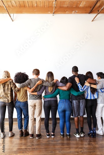 Wallpaper Mural A diverse group of people standing together, arms linked, facing away. Unity and diversity in this group photo, emphasizing togetherness and support. Diverse people standing together as community. Torontodigital.ca