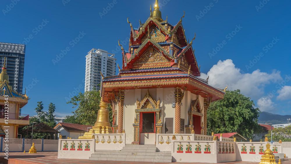 Naklejka premium Beautiful Thai Buddhist ancient temple. Bright colorful roof with golden ornaments, triangular cornices. A shining spire against the blue sky, clouds. Stone steps, fences.Skyscrapers in the distance