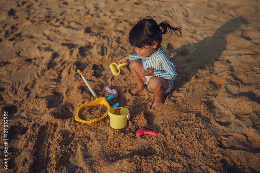 Naklejka premium happy toddler baby girl playing sand toy on sea beach in Pattaya, Thailand