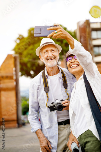 Closeup American senior tourist man with his Asian friend take a photo selfie on blurred of ancient city gate and sun bright background. Senior tourist concept