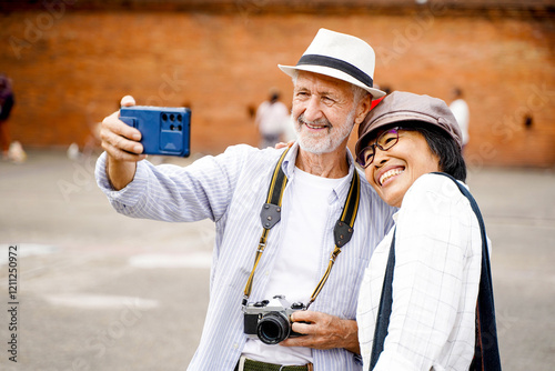 Closeup American senior tourist man with his Asian friend take a photo selfie on blurred of ancient city gate and sun bright background. Senior tourist concept