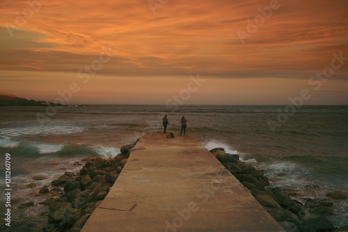 silhouette of two unrecognizable women fishing on a pier at sunset photo