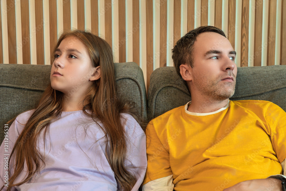 difficult relationship between the father and the daughter of a teenager. Man and the girl are sitting on the couch in the living room, look in different directions. The concept of a quarrel.