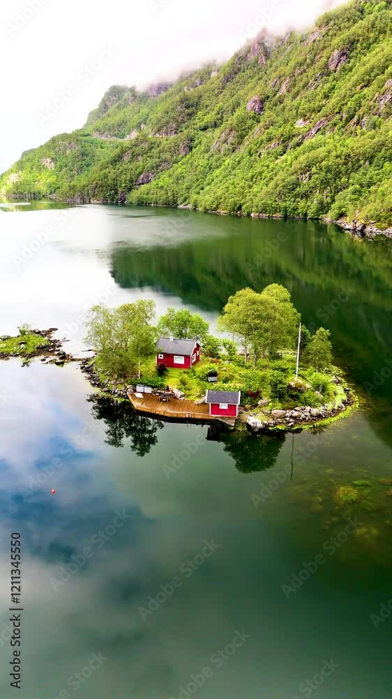 Discover two charming red cabins peacefully located on a small island surrounded by tranquil waters and lush green hills in Lovrafjorden Norway. Embrace the beauty of natures splendor.