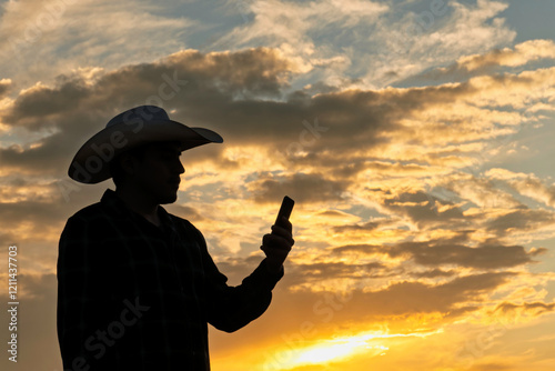 Mexican Cowboy in silhouette holding a phone against a sunset sky