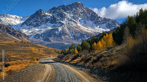 Scenic gravel road leads through autumn landscape and majestic snow-capped mountains under a clear blue sky in a National Park