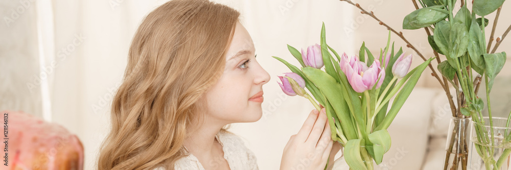 A girl with long hair in a light dress is sitting at the Easter table with cakes, spring flowers and quail eggs. Happy Easter celebration. A girl with long hair in a light dress is sitting at the Easter table with cakes, spring flowers and quail eggs. Happy Easter celebration.