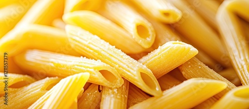 Close-up of uncooked penne pasta in a warm yellow hue, showcasing tubular shapes and textured surfaces, arranged in a natural stacked position.